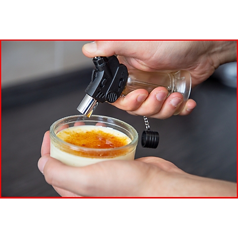 Person flambiert Crème brûlée mit einem Küchenbrenner. Das Dessert befindet sich in einem Glas.